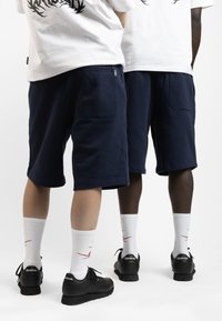 Shorts bleu marine en coton, dotés de poches latérales. Portés avec des chaussettes blanches et des baskets Reebok noires. Design simple et épuré.
