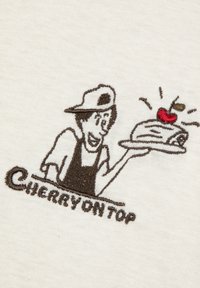 Geborduurd ontwerp van een personage in een pet dat een dessert vasthoudt met een kers erop. Tekst luidt "KERST OP TOP". Kleurenpalet: crème en bruin.