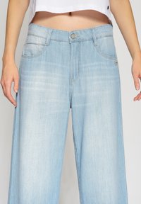 Ljust blå vida jeans med en urtvättad look, som har framfickor, knappstängning och diskreta söm detaljer.