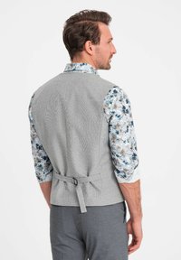 Gray textured vest with a back tie detail, worn over a floral patterned shirt with shades of blue. Slim fit design with defined seams.