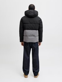 Pūkinis švarkas su didele kapišonu, juoda viršutine dalimi ir pilka apatine dalimi, su skeltukais ir lygiu paviršiumi. Dėvimas su tamsiomis džinsomis.