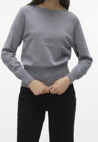 Szary sweter z dzianiny z długimi rękawami, okrągłym dekoltem i prążkowanym dołem, zestawiony z czarnymi spodniami. Gładka faktura, dopasowany krój.