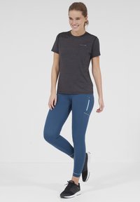 Grå idrottströja med korta ärmar, kombinerad med tajta blå leggings som har en zippered ficka och svarta löparskor.