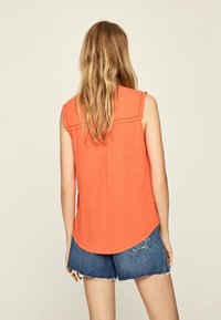 Orange ärmlös topp med volangaxlar och rundad fåll, matchad med fransiga denimshorts. Mjuk tyg med en lätt design.