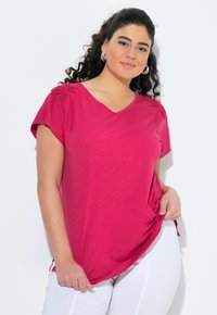 Haut fuchsia à manches courtes avec un col en V, doté de détails texturés aux épaules et d'une coupe décontractée. Associé à un pantalon blanc.