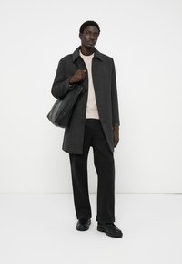 Cappotto grigio a scacchi con colletto, indossato sopra un maglione chiaro, abbinato a pantaloni neri a gamba larga e scarpe nere opache, portando una borsa tote nera.