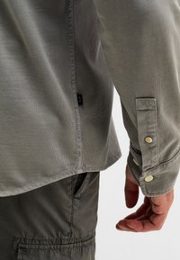 Lichtgrijs overhemd met knopen, een gladde textuur, lange mouwen, een ronde zoom en een geborduurde logotag aan de zijkant.