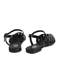 Schwarze Sandalen mit glänzender Oberfläche, ausgestattet mit mehreren Riemen und einer flachen Sohle. Verstellbarer Knöchelriemen mit Schnallenverschluss. Einfaches, offenes Design.