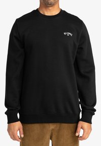 Black sweatshirt with a crew neckline, long sleeves, and ribbed cuffs. Features a small white logo on the chest. Soft texture.