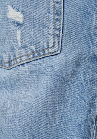 Ljusblå denimtyg med en sliten lapp med fransiga kanter, synlig sömnad och en mjuk textur.