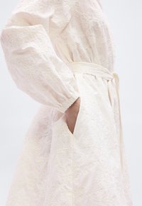 Φόρεμα σε ανοιχτό ροζ χρώμα, κεντημένο με μακριά μανίκια και ζωνάκι στη μέση. Διαθέτει πλαϊνές τσέπες και λεπτά λουλουδάτα σχέδια στο ύφασμα.