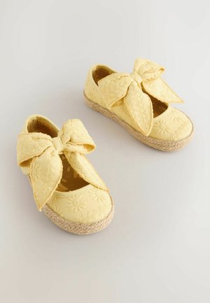Żółte materiałowe buty z dużą kokardą, haftowanym kwiatowym wzorem, okrągłym noskiem i plecioną podeszwą w stylu espadryli.