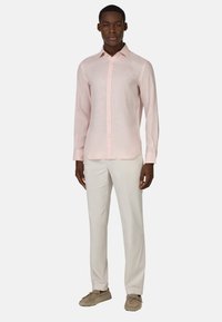 Camicia a maniche lunghe rosa chiaro in lino con bottoni frontali e colletto a punta, abbinata a pantaloni crema e mocassini beige.