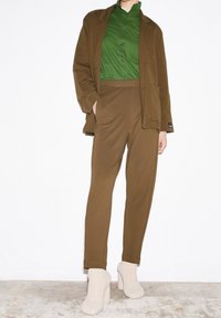 Brązowa marynarka i dopasowane spodnie w połączeniu z zieloną koszulą z guzikami oraz jasnobeżowymi, teksturowanymi botkami na obcasie.