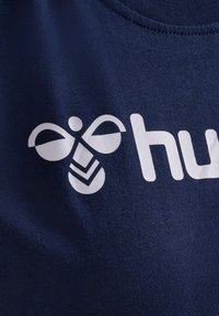 Mörkblått tyg med en vit logotyp som har en stiliserad bi-design och ordet "hu". Texturen verkar slät och mjuk.