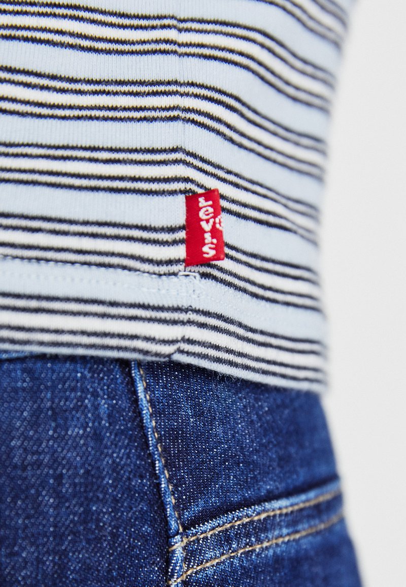 Blau-weiß gestreiftes Hemd mit einem roten Levi's-Etikett, kombiniert mit dunkelblauen Jeans, die Nähte und Texturen zeigen.