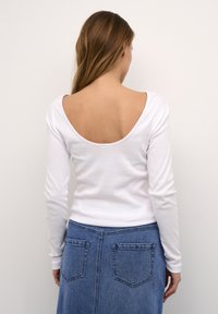 Camiseta de manga larga blanca con un diseño de espalda en forma de scoop, combinada con una falda de mezclilla que cuenta con dos bolsillos traseros y detalles texturizados.