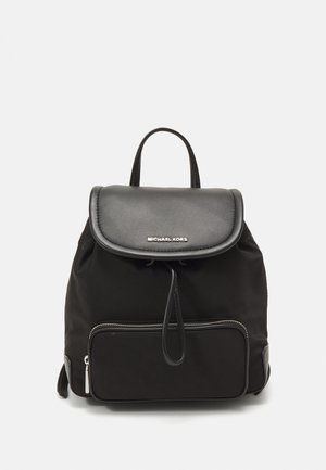 Zwarte Michael Kors rugzak met leren klep en voorvak met rits, verstelbare riemen en handvat aan de bovenkant op een witte achtergrond.
