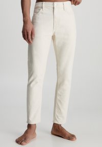 Jeans de mezclilla blancos con un ajuste slim, que cuentan con cinco bolsillos, cierre de botones y costuras visibles a lo largo de las uniones. Cintura plana, sin desgastes.