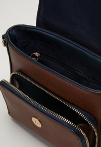 Brązowa skórzana torba na ramię z granatowym wykończeniem, posiada dwie zamykane na zamek przegródki oraz zatrzask w kolorze złotym. Gładka tekstura, kompaktowy design.