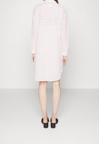 Vestido de color rosa claro con mangas largas, con recortes circulares por todo el diseño. Cuello abotonado y corte relajado, que llega a la mitad del muslo.