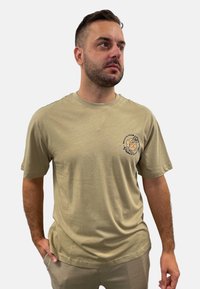 Khaki Baumwoll-T-Shirt mit Rundhalsausschnitt und kurzen Ärmeln, mit einem floralen Motiv auf der linken Brustseite bedruckt. Minimalistisches Design.