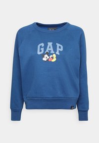 Blå sweatshirt med rund hals och långa raglanärmar. Har en tryckt "GAP"-logotyp och grafik av Mickey Mouse på framsidan. Mjuk textur.