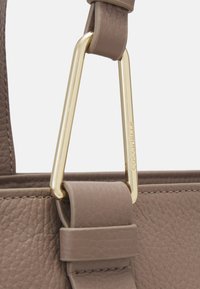 Borsa a mano in pelle marrone con finitura texturizzata, caratterizzata da un accento in metallo dorato e una tracolla con un rivestimento in pelle piatta e liscia.