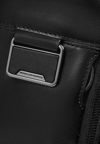 Zwarte leren tas met zilverkleurige metalen accenten en een geperst logo. Het oppervlak heeft een gestructureerde afwerking met zichtbare stiksels.