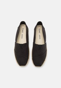 Baskets slip-on en toile noire avec une finition texturée, dotées d'une bande élastique étroite et d'une semelle extérieure en jute naturel. Design classique avec un minimum de détails.