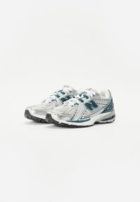 Sport sneakers med en hvit mesh-overdel med teal aksenter, teksturerte paneler og en polstret såle. Snøringer og merkevare er synlige.