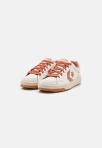 Hvite lær sneakers med rustfargede aksenter, med en stjerne logo og flate rustfargede lisser. Teksturert tåhette og gummisåle.