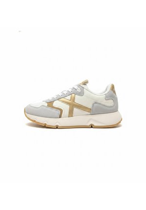 Biały i szary sneaker z złotym wzorem krzyża, białe sznurowadła, gruba biała podeszwa i brązowa podeszwa zewnętrzna widoczna z boku.