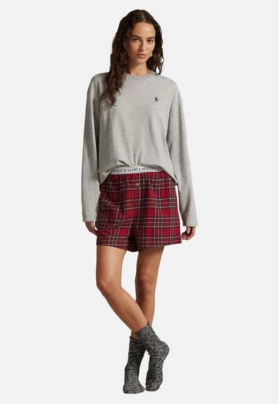 Harmaa pitkähihainen paita logolla, yhdistettynä punaruutuisiin shortseihin, joissa on brändätty vyötärönauha, sekä harmaat neulotut sukat. Sileä ja rento design.