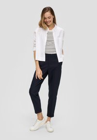 Witte button-up shirt over een zwart-wit gestreepte top, gecombineerd met marineblauwe broek en witte sneakers. Soepele stof, ontspannen pasvorm.