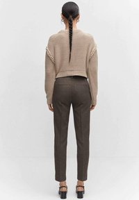 Beige cropped trui met textuurdetails, gecombineerd met bruine op maat gemaakte broeken. De outfit heeft een eenvoudig ontwerp en platte zwarte schoenen.