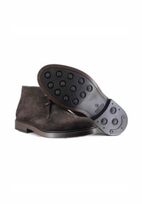 Stivaletti alla caviglia in suede marrone con suola in gomma, caratterizzati da punti di trazione rotondi e rialzati. Design minimalista con finitura liscia e dettagli con lacci.