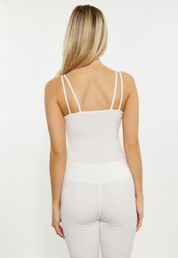Weißes Camisole-Top mit dünnen Trägern, taillierte Passform, glatte Textur. Kombiniert mit hellgrauen Leggings, die ein nahtloses Design an der Taille aufweisen.
