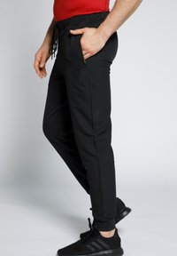 Schwarze sportliche Jogginghosen mit elastischem Bund, Seitentaschen und körpernahem Schnitt. Das Material scheint glatt mit einem dezenten Logo-Design zu sein.