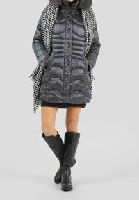 Manteau noir matelassé, écharpe à carreaux gris et bottes noires montantes jusqu'aux genoux. Le manteau possède une fermeture éclair et une capuche.