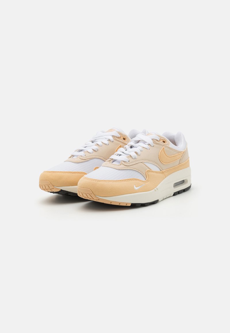 Zapatillas Nike con parte superior de malla blanca, acentos de ante beige, suela acolchada y suela de goma negra. Incluye cordones blancos y logotipo.
