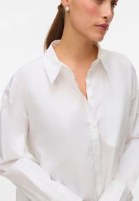 Hvit skjorte med knapp, laget av glatt stoff, med klassisk krage, en brystlomme og lange ermer med brede mansjetter.