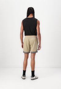 Shorts en maille beige avec taille élastique et rayures noires sur l'ourlet, associés à un haut sans manches noir et des baskets grises.