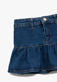Falda de mezclilla en un tono azul oscuro, con un volante acampanado en el dobladillo y lazos para cinturón estándar. Las costuras en contraste añaden detalle.
