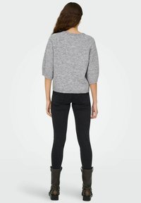 Grijze gebreide trui met een relaxte pasvorm en driekwartmouwen, gecombineerd met zwarte skinny jeans en kniehoge laarzen.