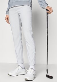 Ljust grå golfbyxor har en strömlinjeformad design med en slät textur, i kombination med vita träningsskor och en golfklubba.