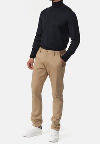 Beige chino's met een rechte pasvorm, voorzien van voorzakken, ceintuurlussen en een knoopsluiting, gecombineerd met een zwarte coltrui en witte sneakers.