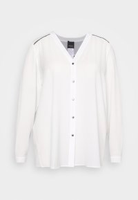 Blusa bianca a maniche lunghe con scollatura a V, chiusura con bottoni e dettagli decorativi sulle spalle, su uno sfondo semplice.