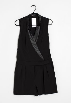 Schwarzer ärmelloser Overall mit Satin-Reverskragen und plissierten Shorts, der an einem schwarzen Bügel vor weißem Hintergrund hängt.