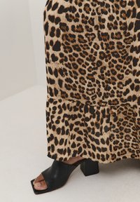 Suknja midi dužine s uzorkom leopard, s volanima na rubu, izrađena od mekog materijala. Uparena s crnim sandalama na blok petu s otvorenim prstima.